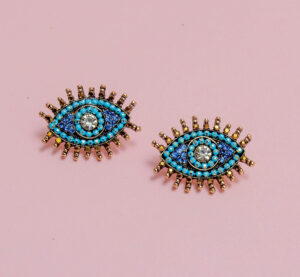 Blue beaded earrings with eye motifs on a pink background.