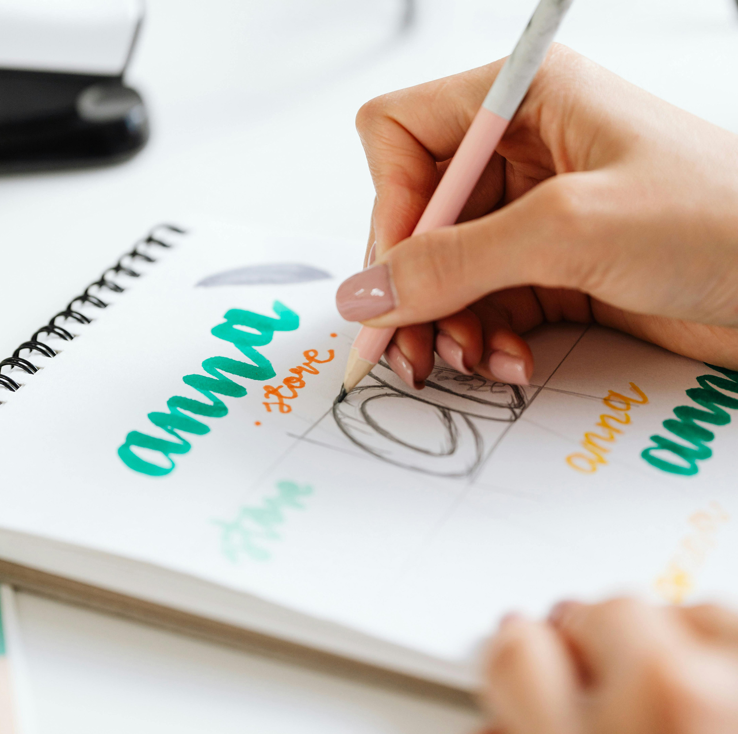 Worldwide business branding solutions Close-up of a hand sketching a logo in a notebook with colored markers, highlighting adamanto’s brand identity design services.