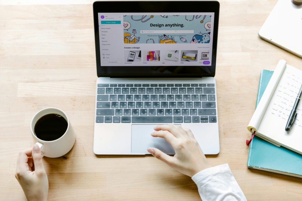 Desk with a laptop showing canva.com, a coffee mug, and a notebook with notes, illustrating the mistakes small businesses make when designing logos on Canva.