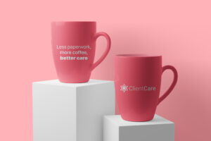 Pink mugs featuring ClientCare’s logo and the phrase "Less paperwork, more coffee, better care."