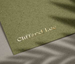 Textured green paper with Clifford Lee’s logo embossed in foil, with plant shadow detail.