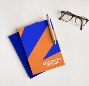 Branded Contacto Visual notebook with white logo and corporate texture, placed next to eyeglasses on a white surface.