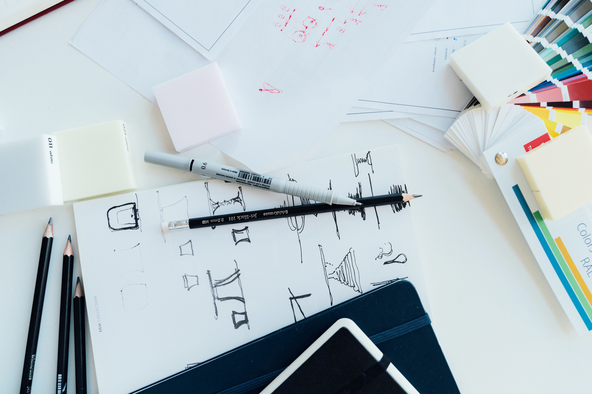 Desk with logo sketches, pencils, pens, and open Pantone books, illustrating the difference between a logo and a brand identity.