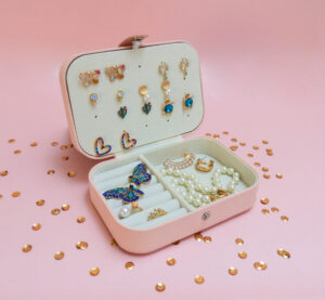 Pink jewelry box with adara earrings, rings, and necklaces on a pink background.