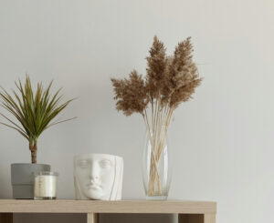 Minimalist home decor with a scented candle, ceramic sculpture, and a green plant on a wooden table.