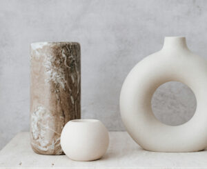 Two ceramic vases in neutral tones with a white spherical candle on a light background.