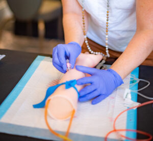 Midwifery training session with a woman practicing intravenous line application on a mannequin.