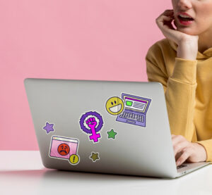 Woman in yellow hoodie typing on a laptop with Angie Contreras branding stickers.