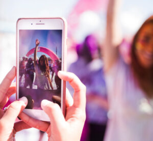 Woman photographing another at a feminist march with purple flags in the background.