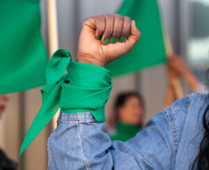 Woman's fist with green scarf in a feminist protest, symbolizing solidarity for women's rights.