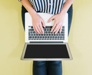 Woman typing on a laptop against a yellow background, symbolizing modern digital engagement.