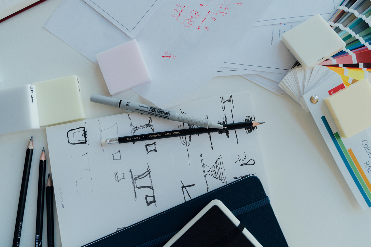 A desk with logo sketches, pencils, a Pantone swatch book, and design materials, illustrating the creative process of finalizing a logo.