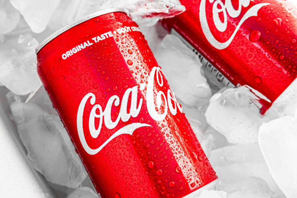 Two Coca-Cola cans on ice with water droplets, featuring the classic white script logo on a red background, demonstrating the impact of typography in branding.