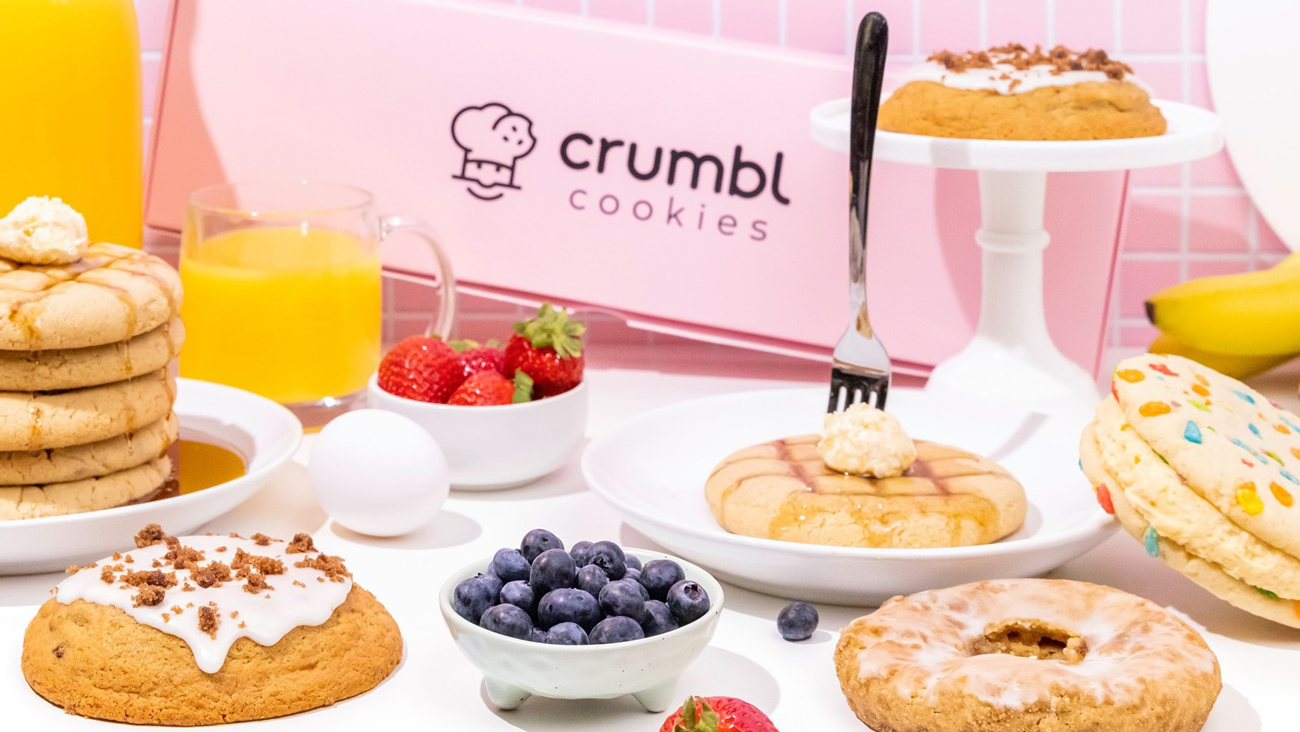 A table with Crumbl Cookies, fresh fruits, eggs, and juice, featuring the brand's signature pink packaging and logo in the background. brand that connects with your audience