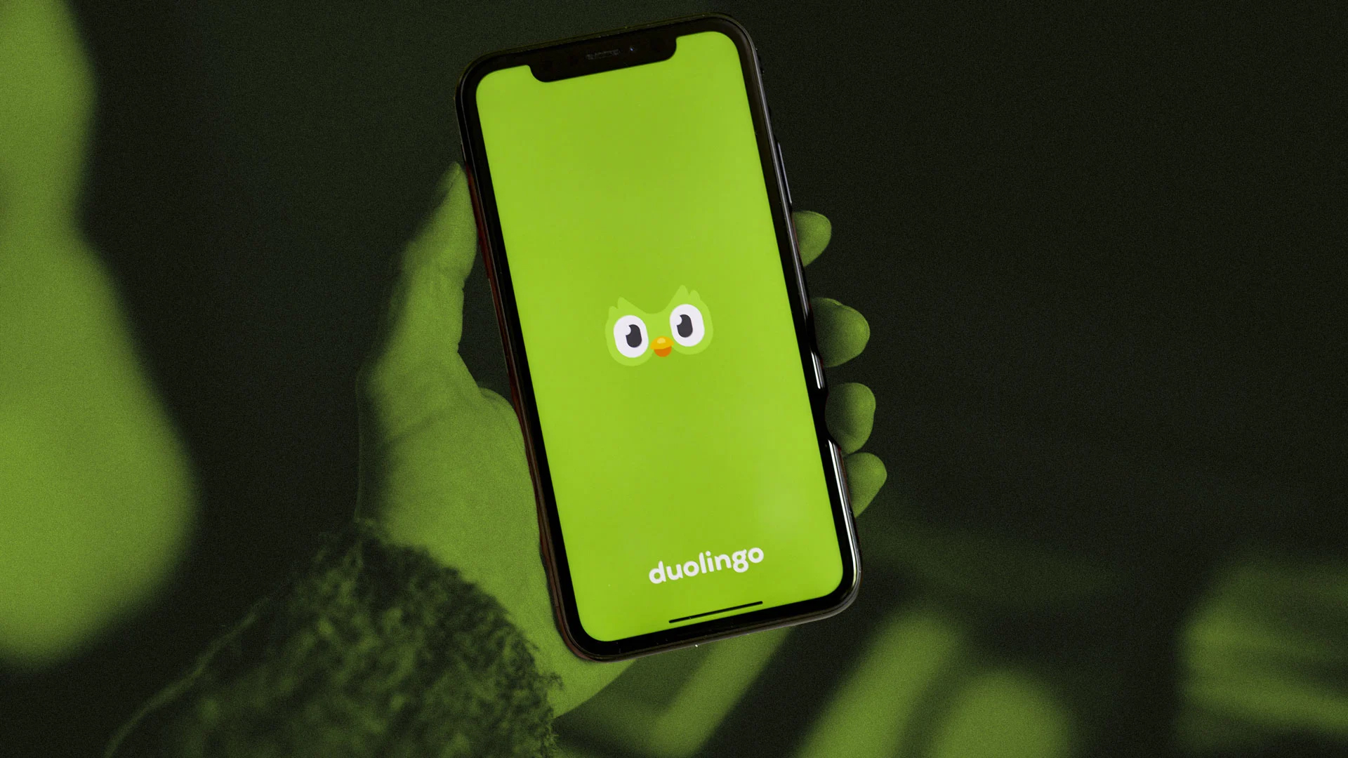 Hand holding phone with Duolingo app open, demonstrating brand consistency on social media with cohesive green branding.