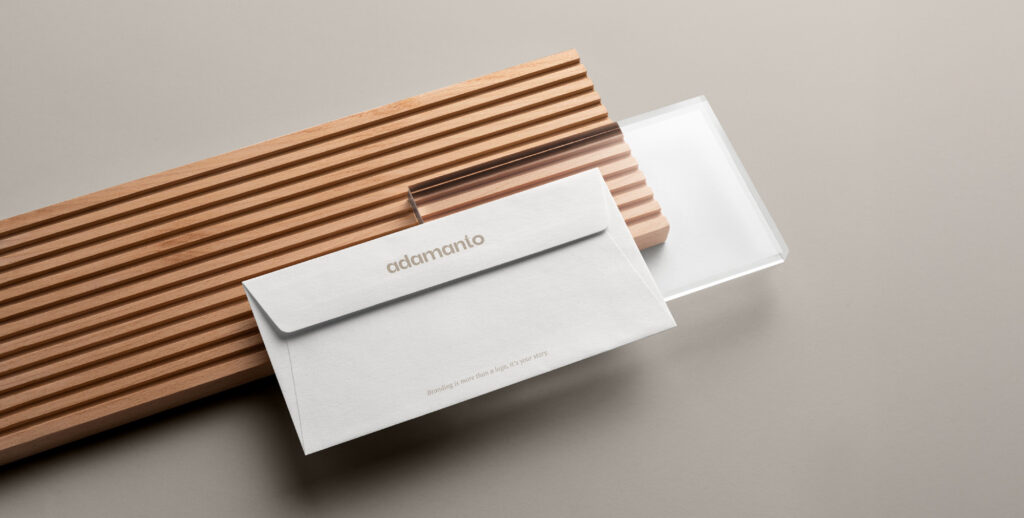 Branded envelope with adamanto logo and tagline on a wooden and glass surface.