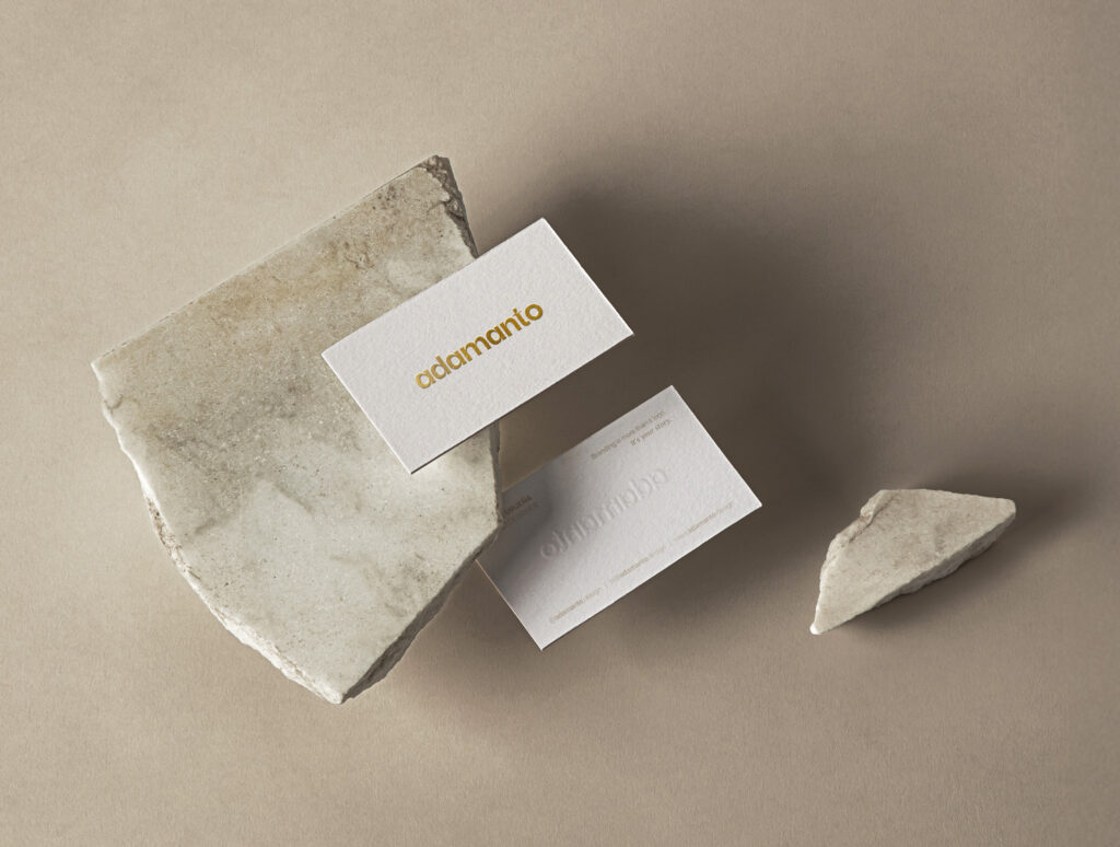 Business cards for adamanto, a brand identity for creative studio, with gold foil hot stamping and elegant beige stone background.