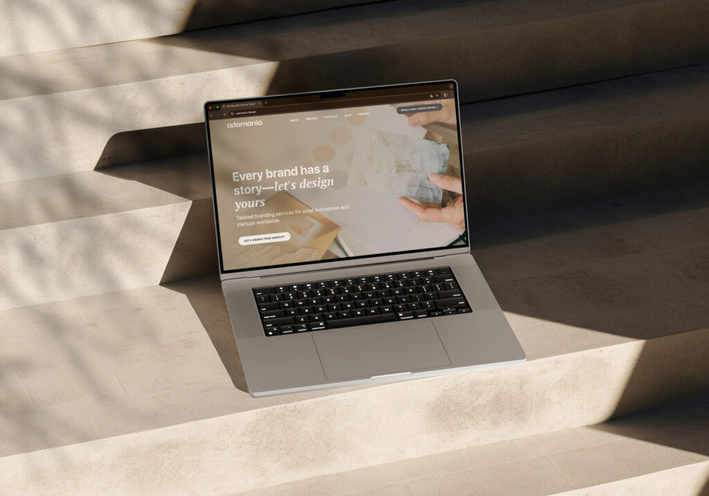 MacBook placed on beige stairs displaying adamanto’s homepage with main header.